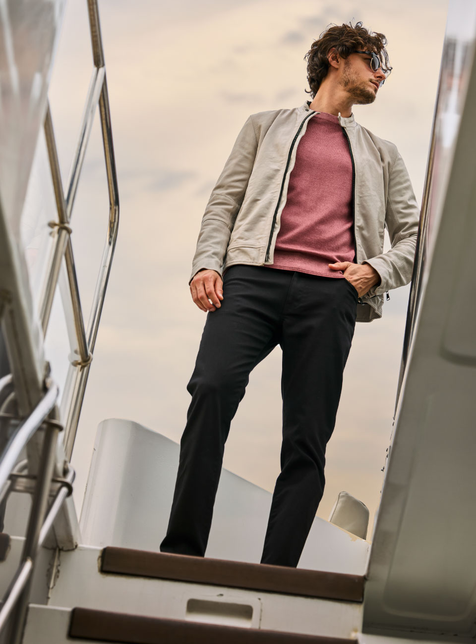 ライトピンクのトップス・アイボリーのジャケット・ブラックのデニムパンツを着用した男性が手をポケットに入れて遠くを見ている様子