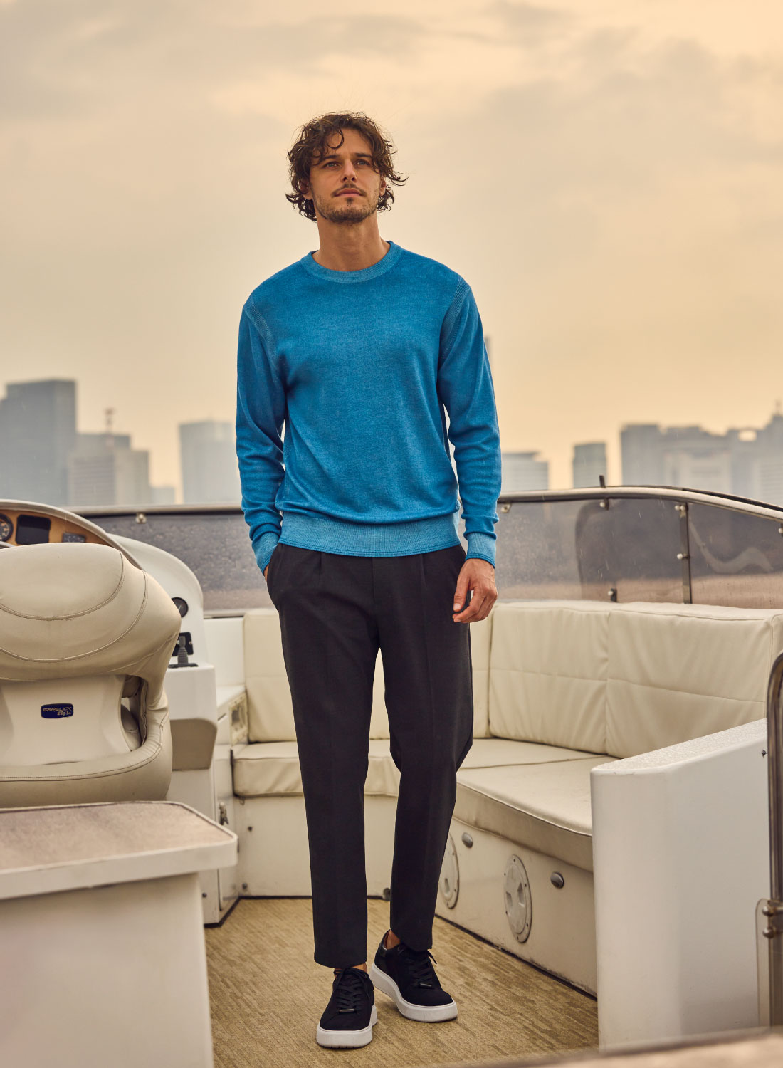 ブルーのトップス・ブラックのパンツを着用した男性が船の上で遠くを眺めている様子