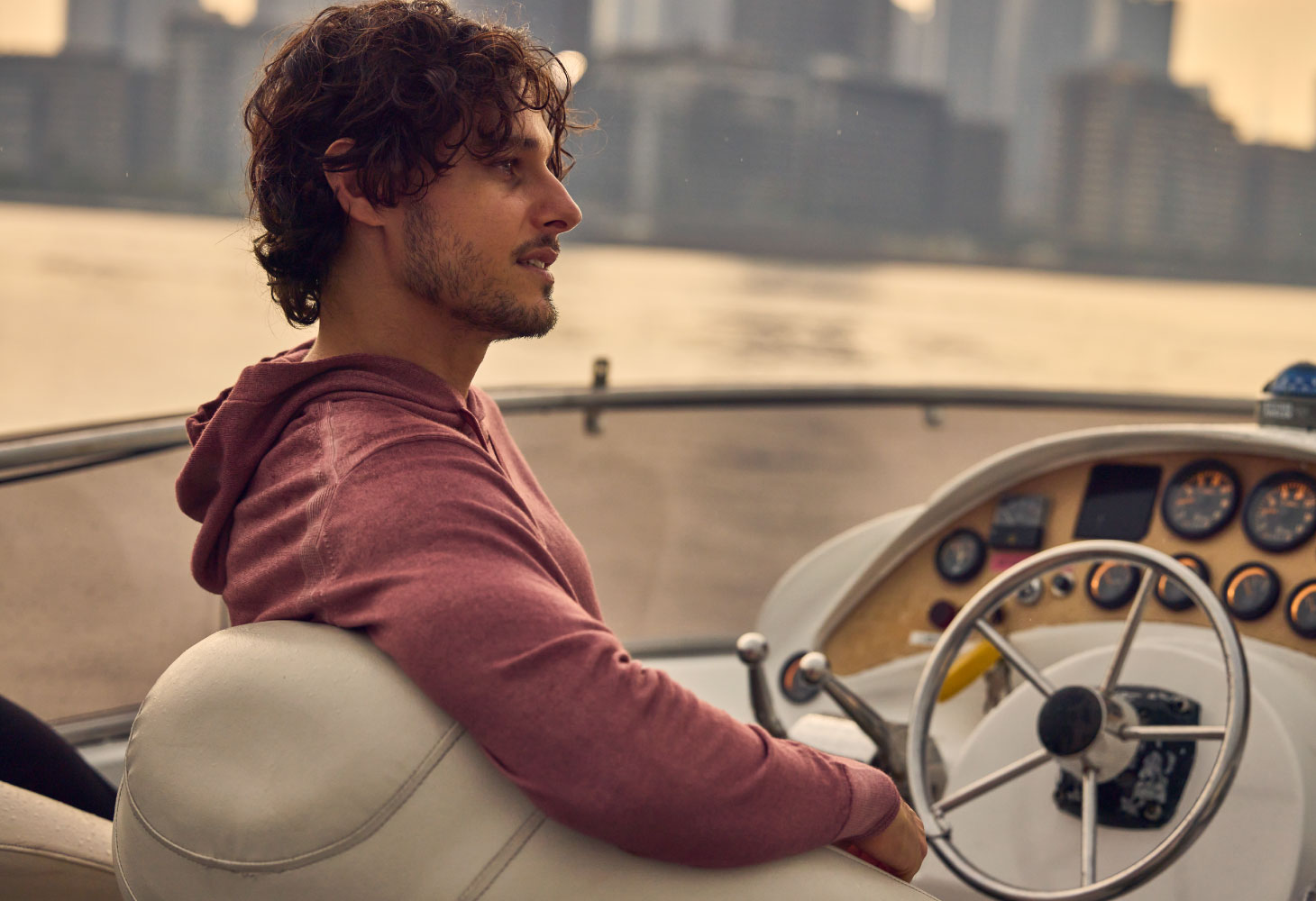 ライトピンクのパーカーを着用した男性が船の操縦席に座って遠くを眺めている様子