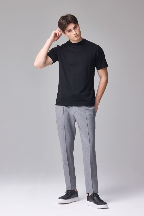 黒の半袖Tシャツとグレーのパンツを着用し、頭に手を添える男性の正面姿