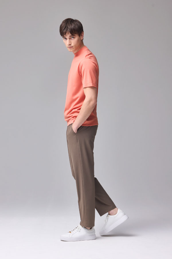 サーモンピンクの半袖Tシャツとブラウンのパンツを着用した男性の横向き姿
