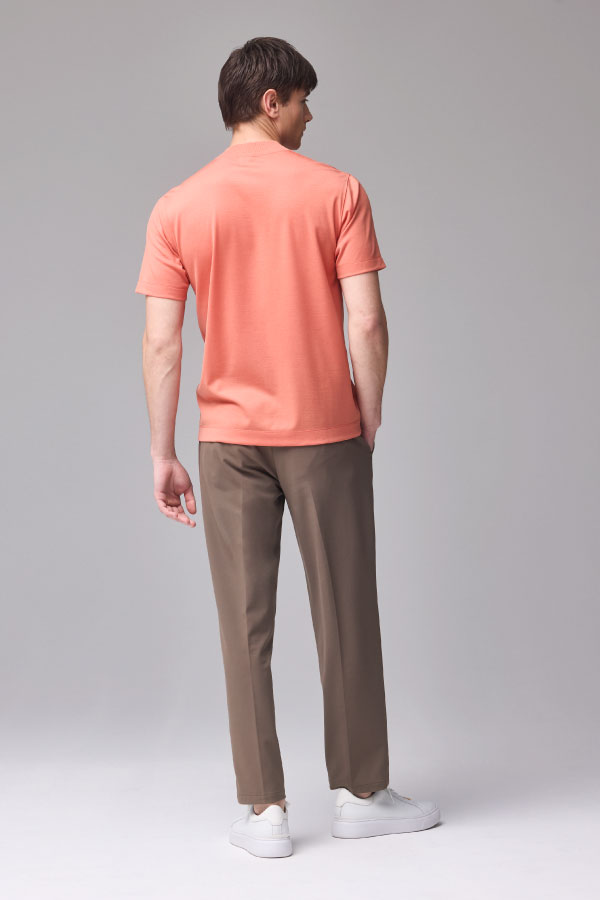 サーモンピンクの半袖Tシャツとブラウンのパンツを着用した男性の後ろ姿